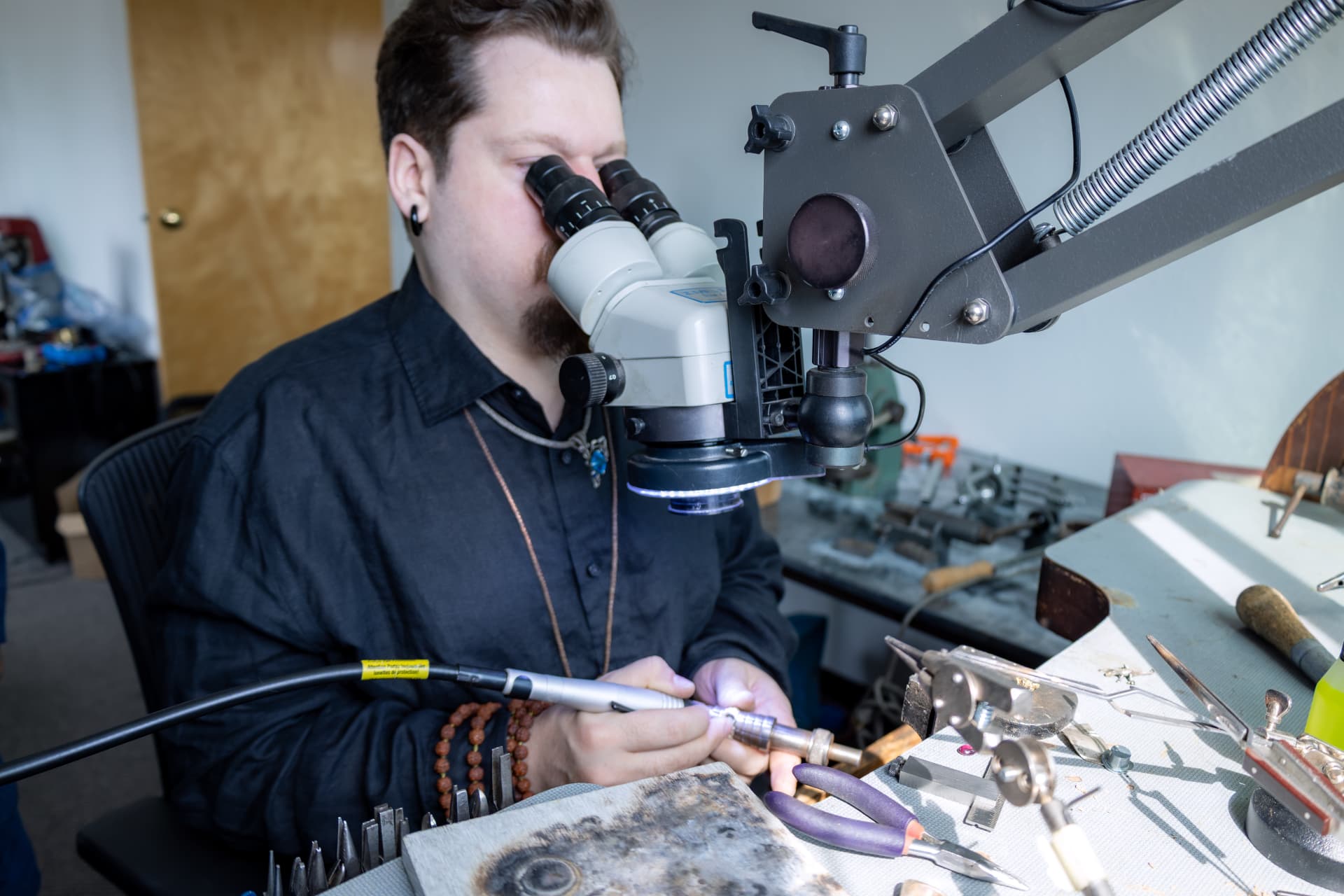 A jeweler at the bench working under a microscope